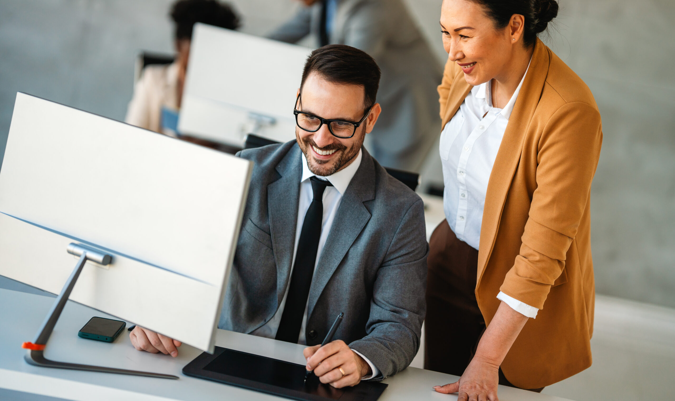 Senior business manager talking with experienced colleague while using computer in office. Financial and marketing projects. Specialists work in diverse team.